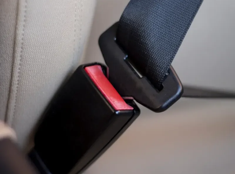 Black seat belt buckle receiver with a red release button mounted beside a beige vehicle seat