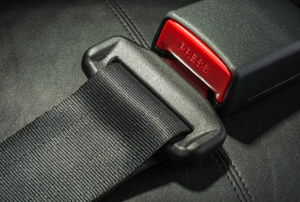 Grey retractable seat belt webbing engaged in a black buckle with a red press-release button