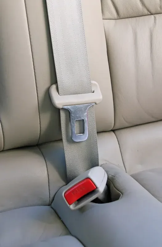 Three-point seat belt routed diagonally across the backrest of a light-coloured rear car seat