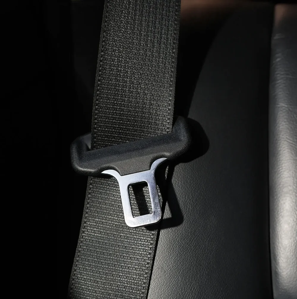 Close detail of seat belt webbing running through a metal latch plate
