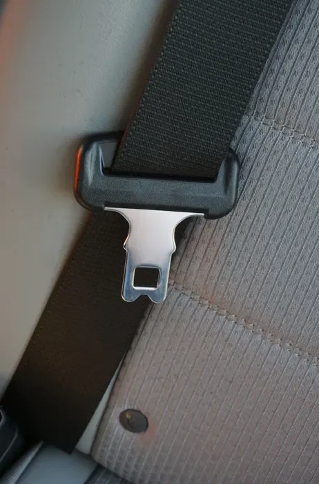 Seat belt webbing and latch plate shown against the fabric of a vehicle seat
